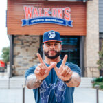 NFL Quarterback Dak Prescott does the W hand sign in from of a Walk-On's restaurant wearing the navy WIN tee and the W snapback hat.