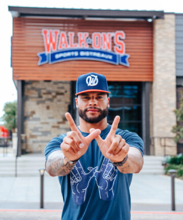 NFL Quarterback Dak Prescott does the W hand sign in from of a Walk-On's restaurant wearing the navy WIN tee and the W snapback hat.
